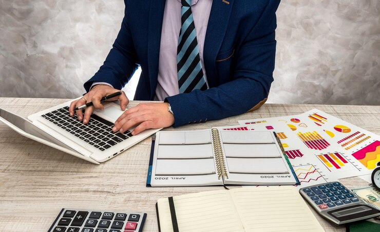 Businessman working in office with business graphs, laptop and notepad.